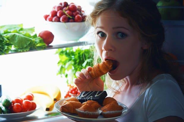 Woman eating junk food from an open fridge. 
